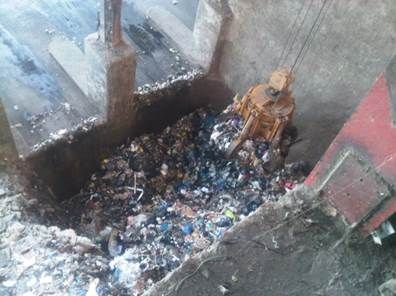 Compacteur à déchets rempli de déchets mélangés ; machines métalliques au-dessus.