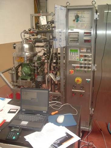 Machine industrielle avec jauges, vannes et panneau de commande. Un ordinateur portable et des documents sont à l'avant.