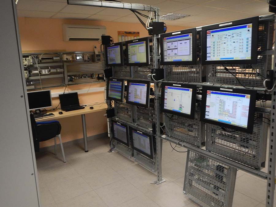 Salle de contrôle avec plusieurs écrans affichant des données. Matériel informatique, bureau et étagères présents.