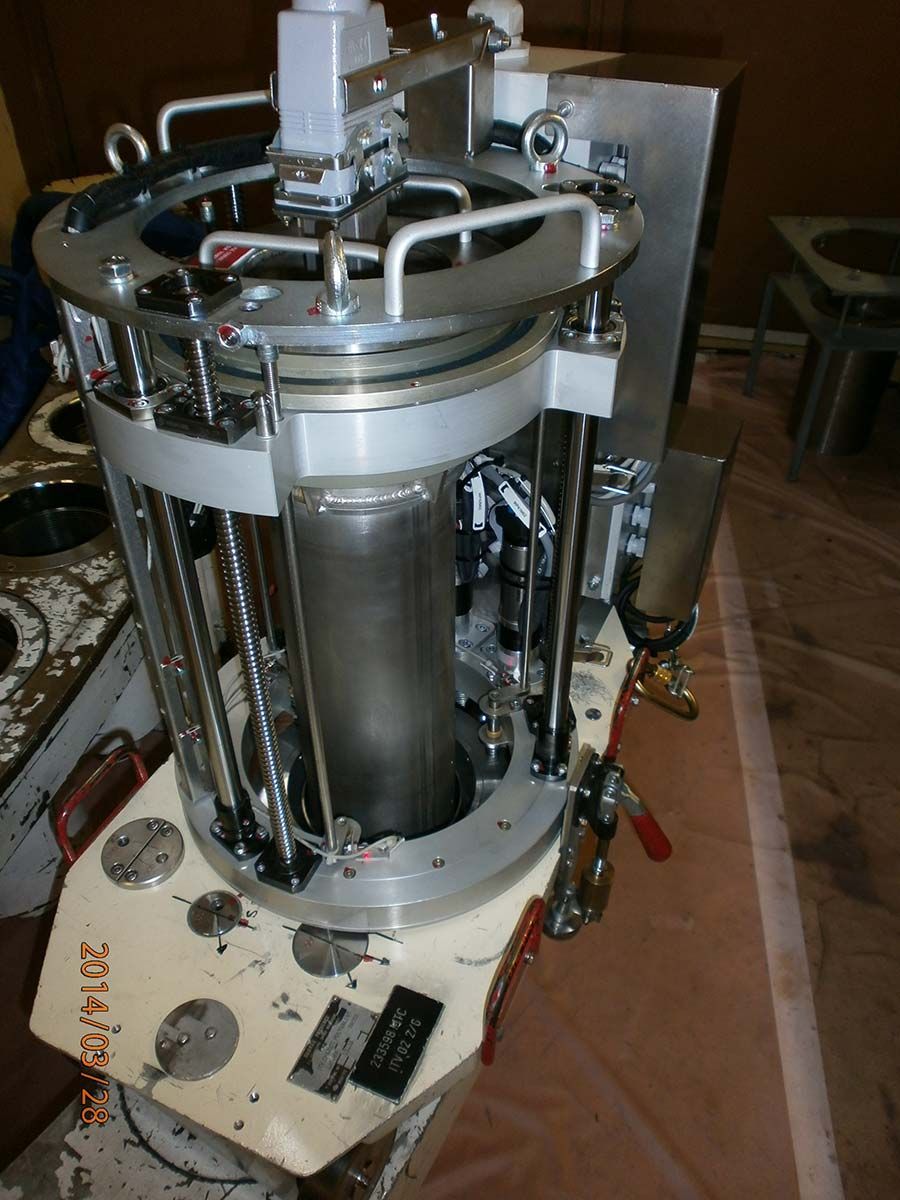 Un dispositif cylindrique en métal, probablement destiné à un usage industriel, repose sur une surface, avec divers tuyaux et tiges visibles.