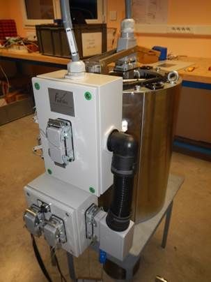 Un appareil cylindrique en acier inoxydable avec des boîtiers électriques, des tubes et des câbles attachés, posé sur une table en métal.