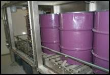 Barils violets sur un tapis roulant dans un environnement industriel.