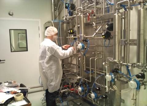 Personne en blouse de laboratoire réglant les vannes d'un système complexe de tuyauterie en acier inoxydable dans une salle stérile.