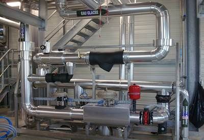 Tuyaux et équipements industriels, argentés et rouges, avec un escalier en arrière-plan.