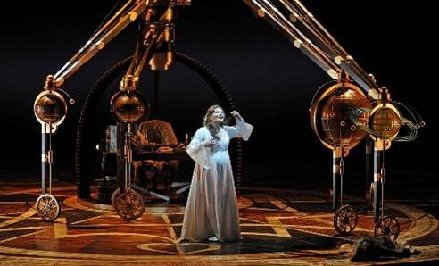 Femme chantant sur une scène avec des machines steampunk ornées dans un théâtre sombre.