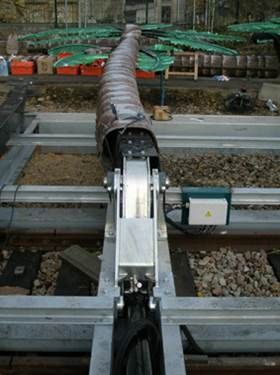 Câble et appareil métalliques au-dessus des voies ferrées. Revêtement marron avec des extensions vertes en forme de palmier dans une gare de triage.