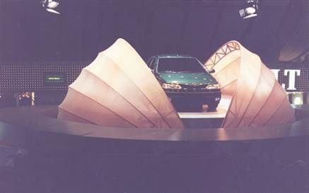 Voiture verte sur une scène encadrée de grandes structures en forme de coquillage de couleur claire ; décor sombre.