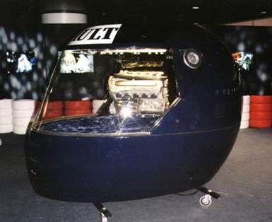 Une grande machine bleu foncé en forme de casque avec un cockpit transparent affichant un moteur sur roues.