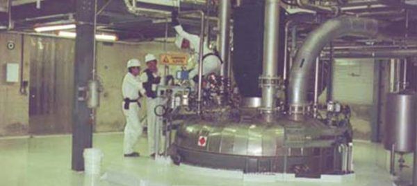 Trois ouvriers portant des combinaisons de protection blanches et des casques examinent de gros équipements industriels dans un laboratoire.