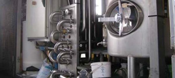 Équipement industriel en acier inoxydable avec tuyaux et un grand récipient cylindrique.