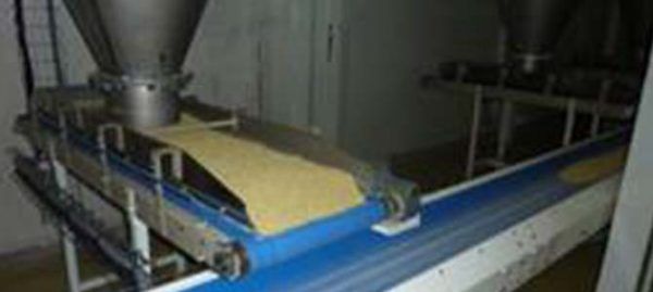 Un système de bande transporteuse dans une usine, distribuant une couche de substance jaune.