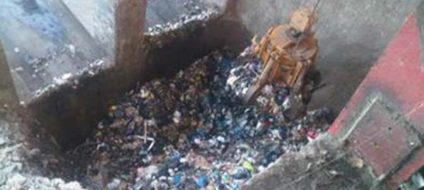 Une machine industrielle ramasse les déchets d'une grande fosse, filmée sous un angle élevé.