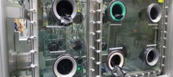 Boîte à gants avec plusieurs ports pour les bras, utilisée en laboratoire. Transparente, rectangulaire, avec des gants s'étendant vers l'intérieur.