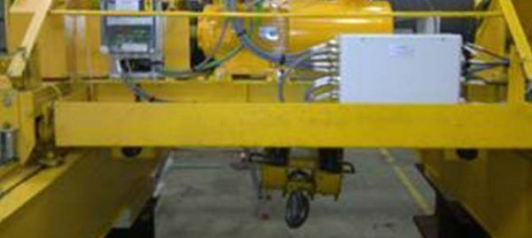 Machine industrielle jaune avec un composant en forme de boîte suspendu au-dessus d'une surface.