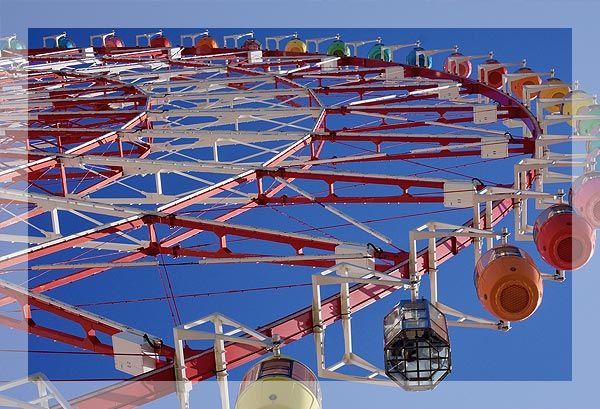 Grande roue avec cadre rouge et blanc, voitures colorées sur fond de ciel bleu.