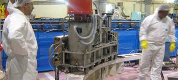 Deux personnes en costumes blancs près de machines, avec un haut rouge dans un décor d'usine.