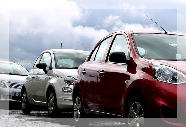 Voitures garées en rangée, avec une voiture rouge au premier plan, ciel nuageux en arrière-plan.