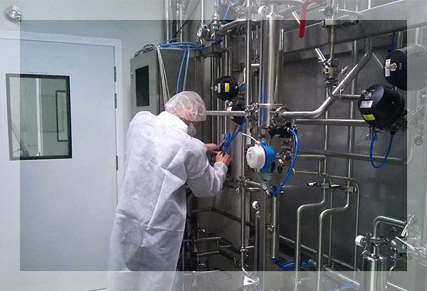 Une personne portant une blouse blanche et un filet à cheveux travaillant sur des tuyaux en acier inoxydable dans une salle blanche.