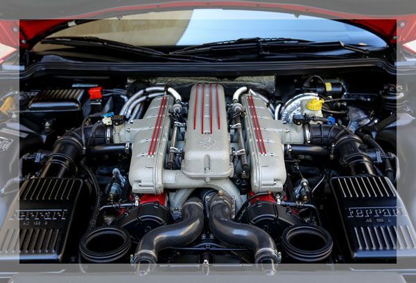 Gros plan d'un moteur Ferrari, composants argentés et rouges, dans le compartiment moteur d'une voiture.