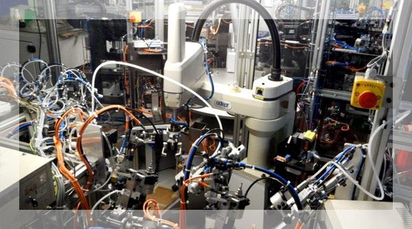 Bras robotisé dans une usine, entouré de machines, de tubes et de fils, pour l'assemblage automatisé.