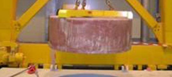 Un grand cylindre rose est suspendu par une grue industrielle jaune.