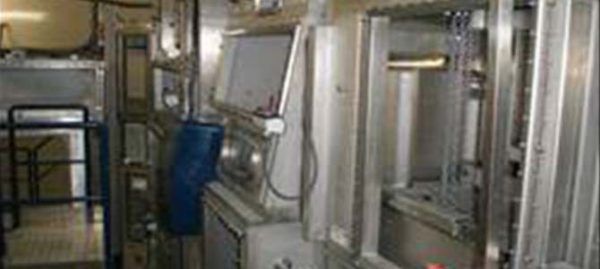 Un intérieur industriel avec des machines et des équipements en acier inoxydable. Un tonneau bleu est accroché au mur.