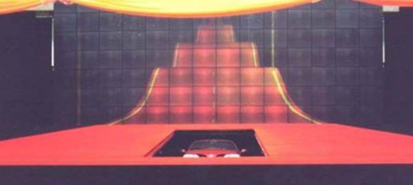 Une voiture rouge sort d'une fosse sur une scène avec un fond lumineux à plusieurs niveaux.