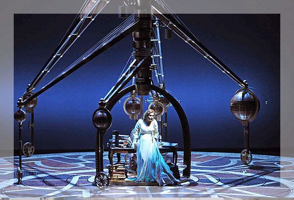 Femme en robe bleue, debout près d'une machine complexe dans un décor sombre et orné.