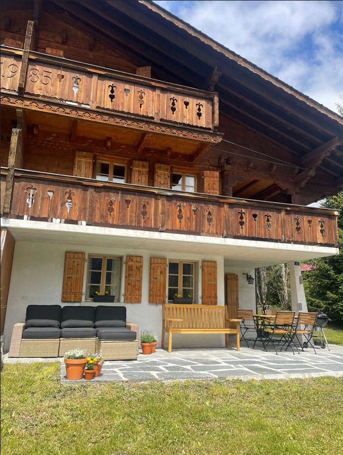 Chalet en bois de deux étages avec balcon, volets et coin salon extérieur sur une terrasse pavée.