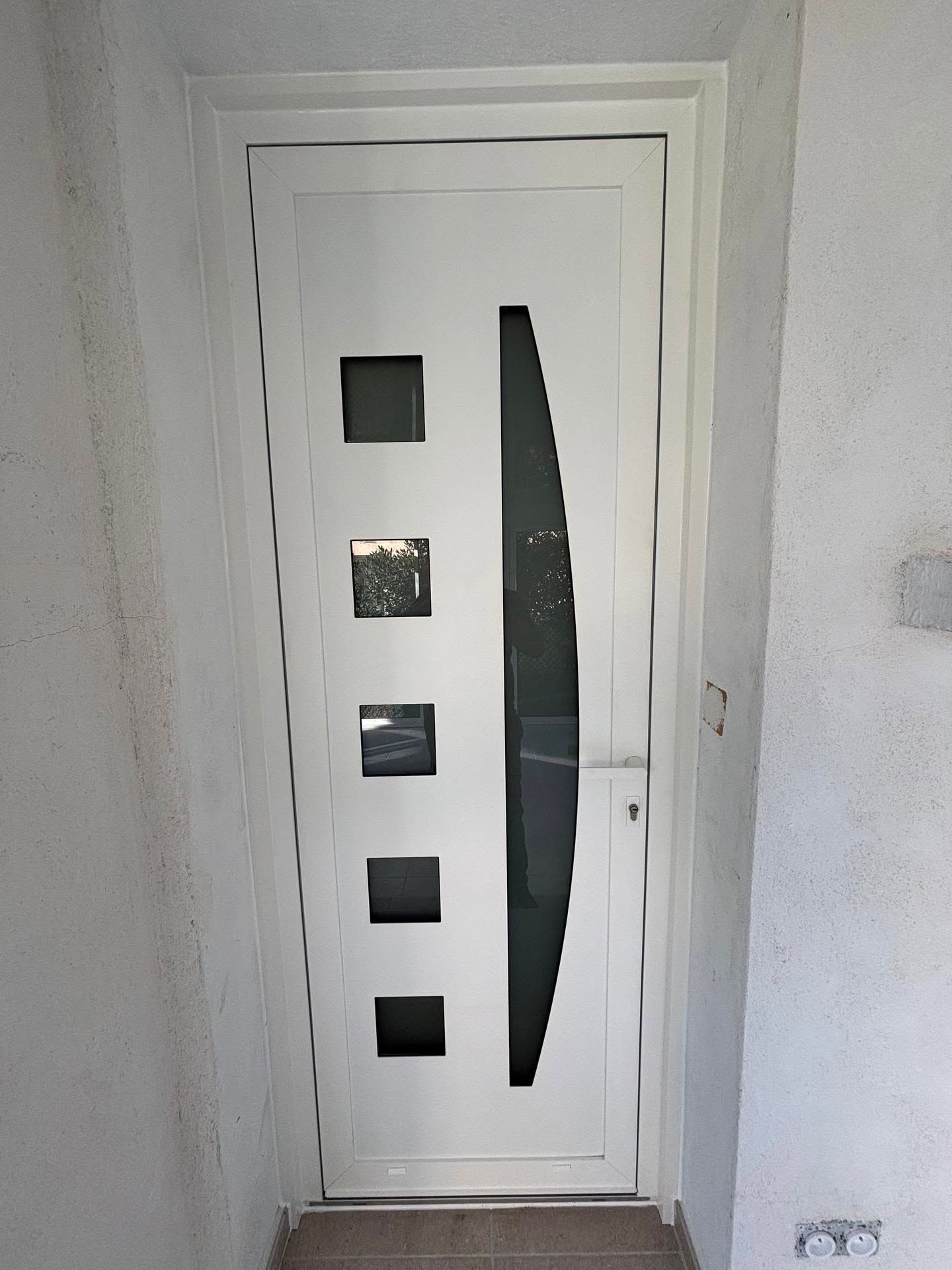 Porte d'entrée blanche avec petites fenêtres carrées et une verticale donnant sur un couloir