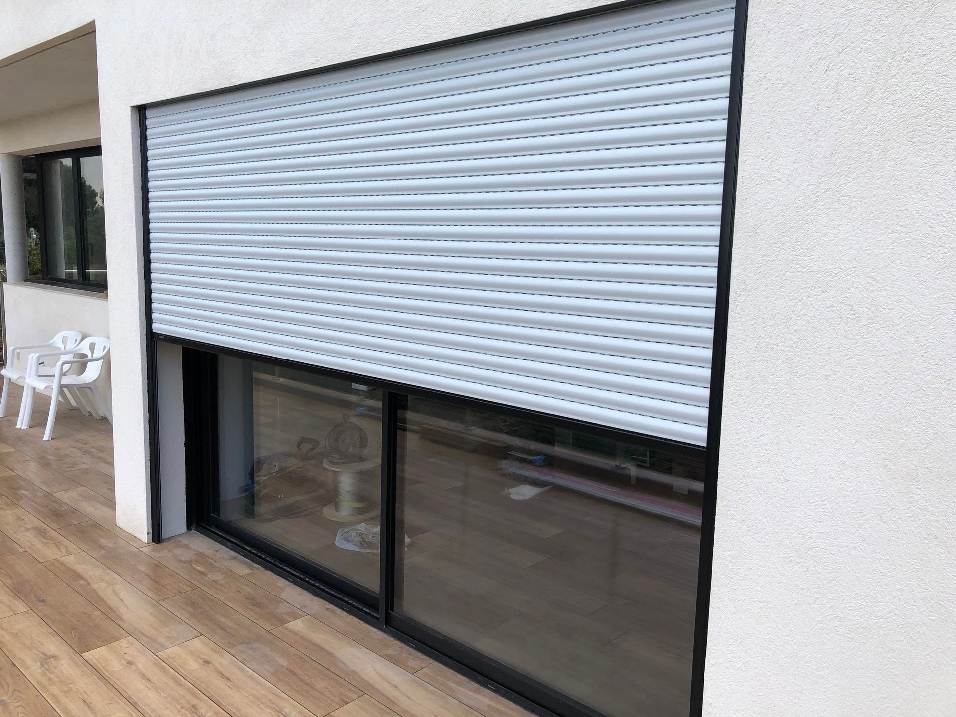 Volet roulant blanc fermé sur une porte vitrée à cadre noir donnant sur une terrasse