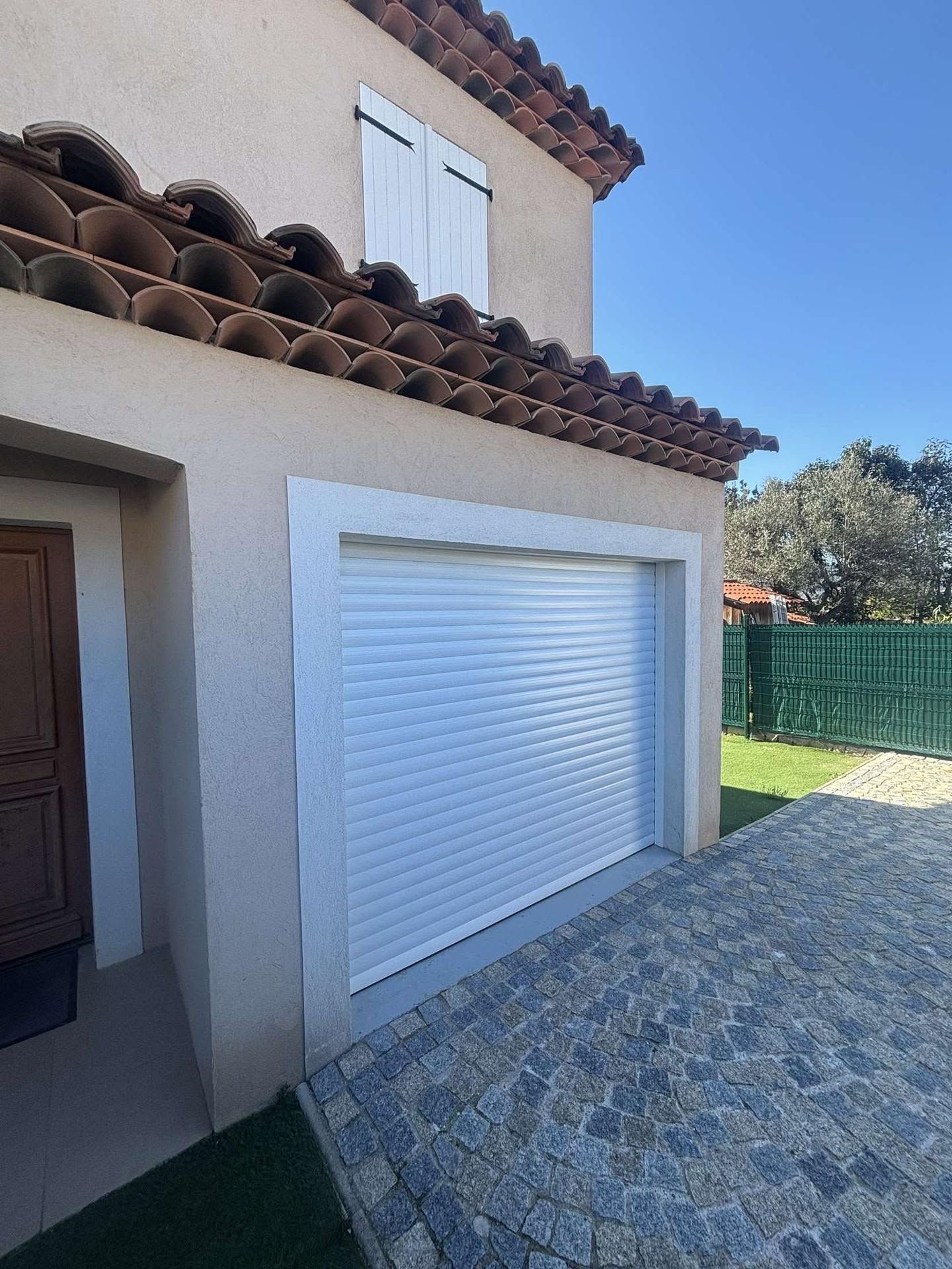 Extérieur de la maison avec porte de garage blanche, toit de tuiles et allée en pierre sous un ciel dégagé