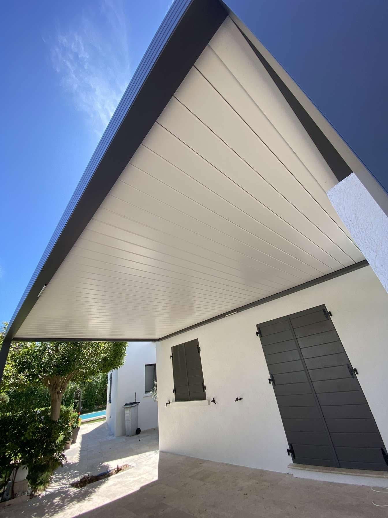 Extérieur d'une maison moderne avec un toit pentu, des murs blancs et des volets sombres sous un ciel bleu