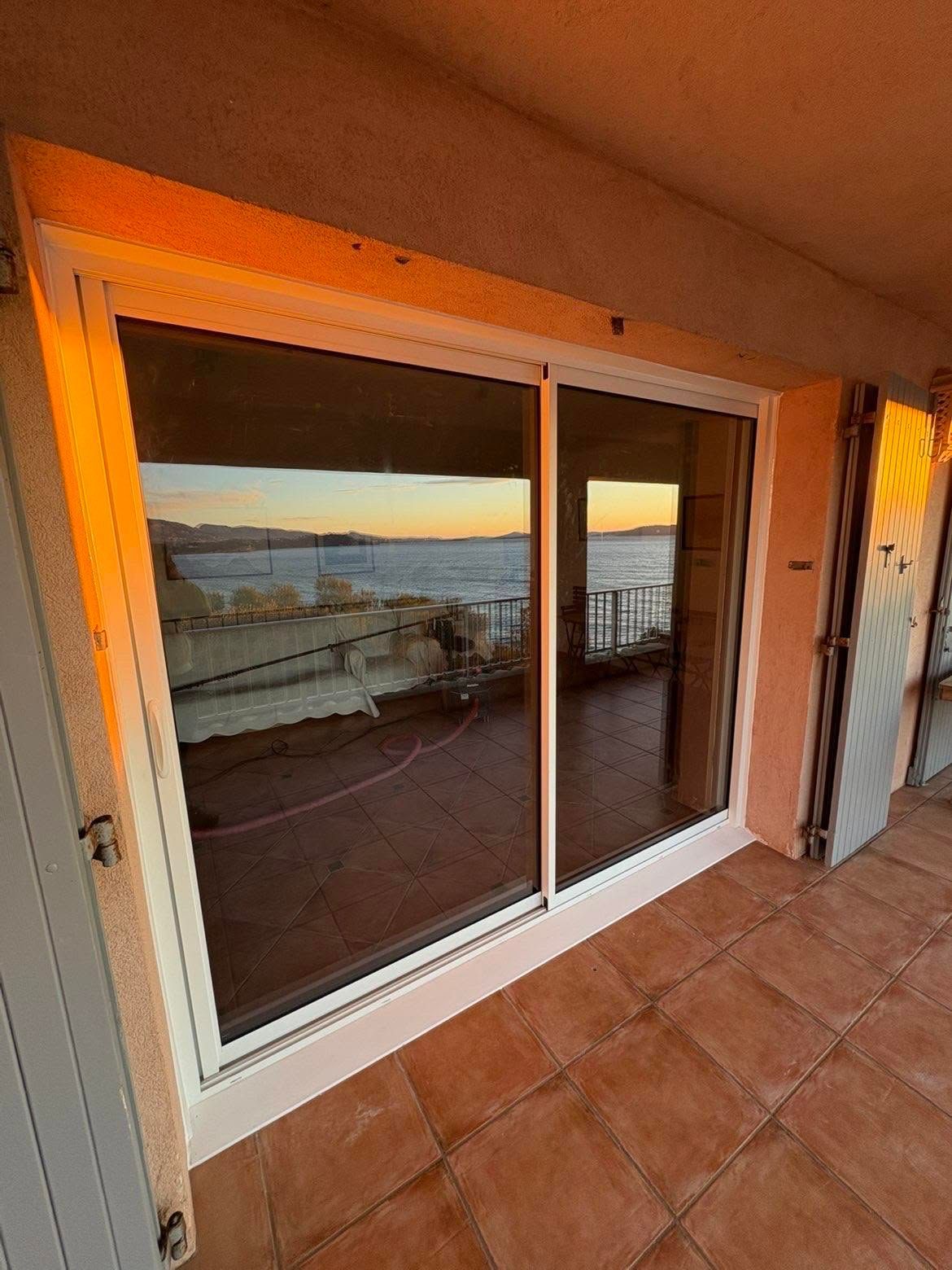 Porte-fenêtre coulissante donnant sur une vue du coucher de soleil depuis une terrasse carrelée