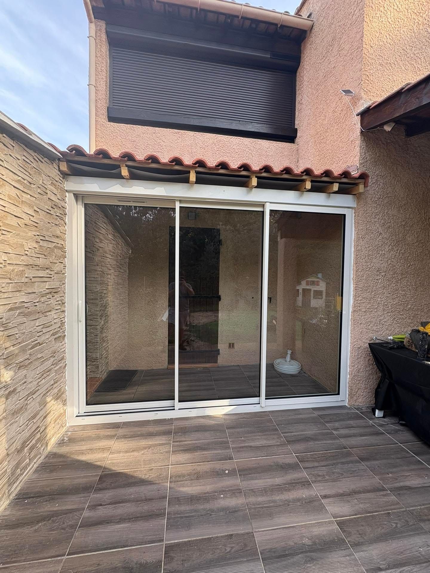 Terrasse arrière avec portes coulissantes en verre blanc et une fenêtre à l'étage, bordée de murs en stuc et d'un sol carrelé foncé
