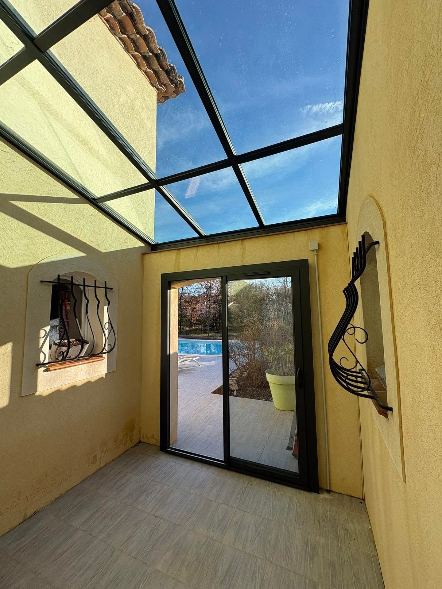 Patio couvert aux murs jaunes, sol carrelé et porte-fenêtre coulissante donnant sur une cour ensoleillée.