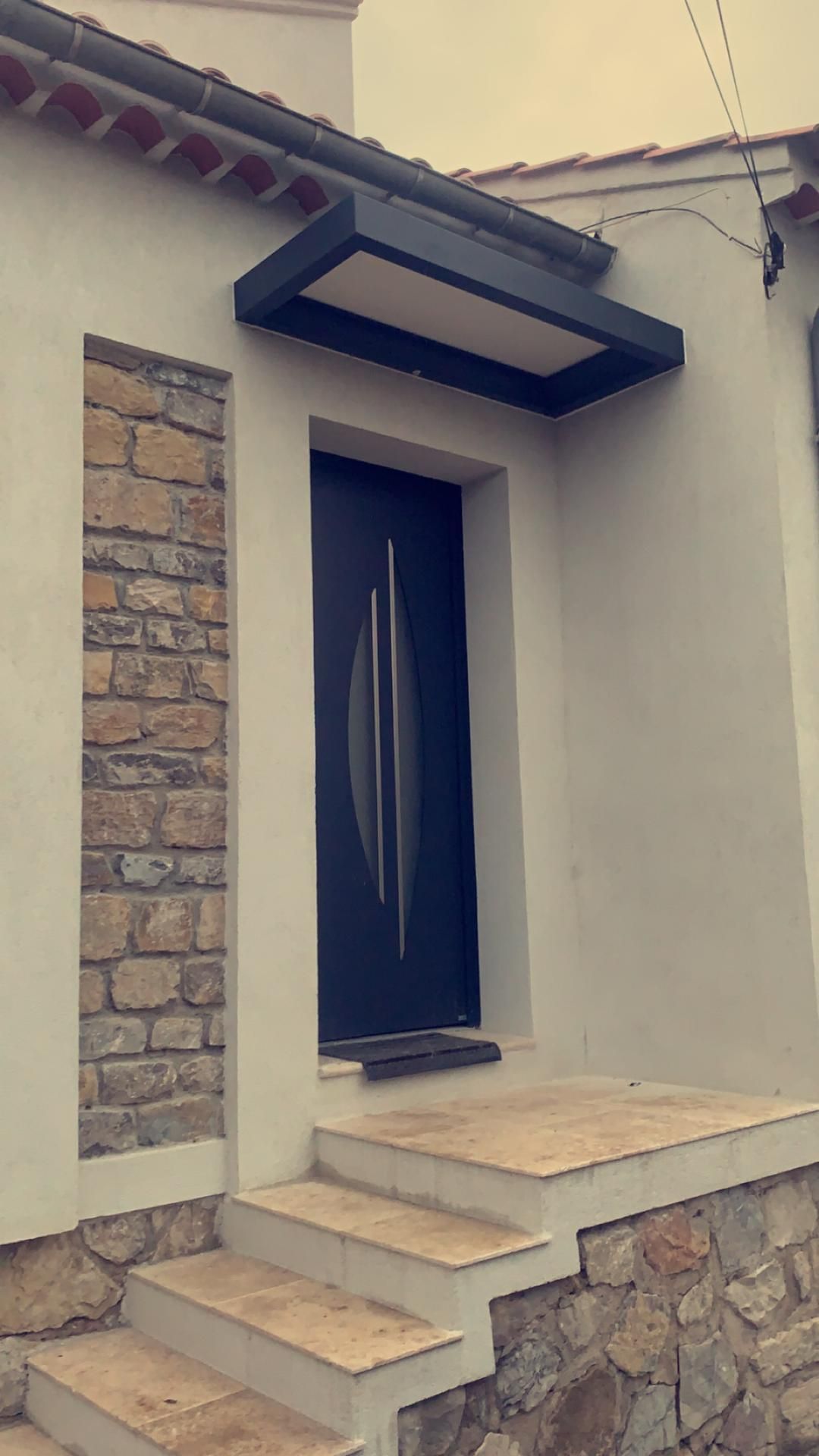 Petite entrée principale avec marches, porte bleue, façade en pierre et auvent en surplomb.
