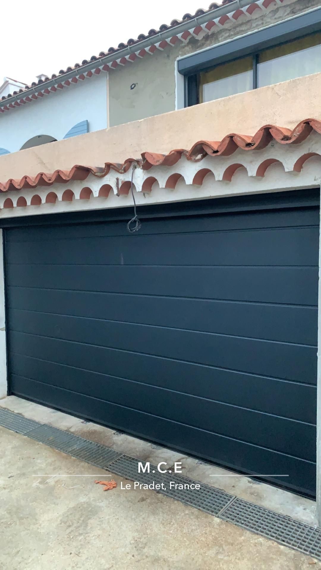 Porte de garage bleu foncé sur une maison avec un mur en stuc beige et une toiture en tuiles rouges