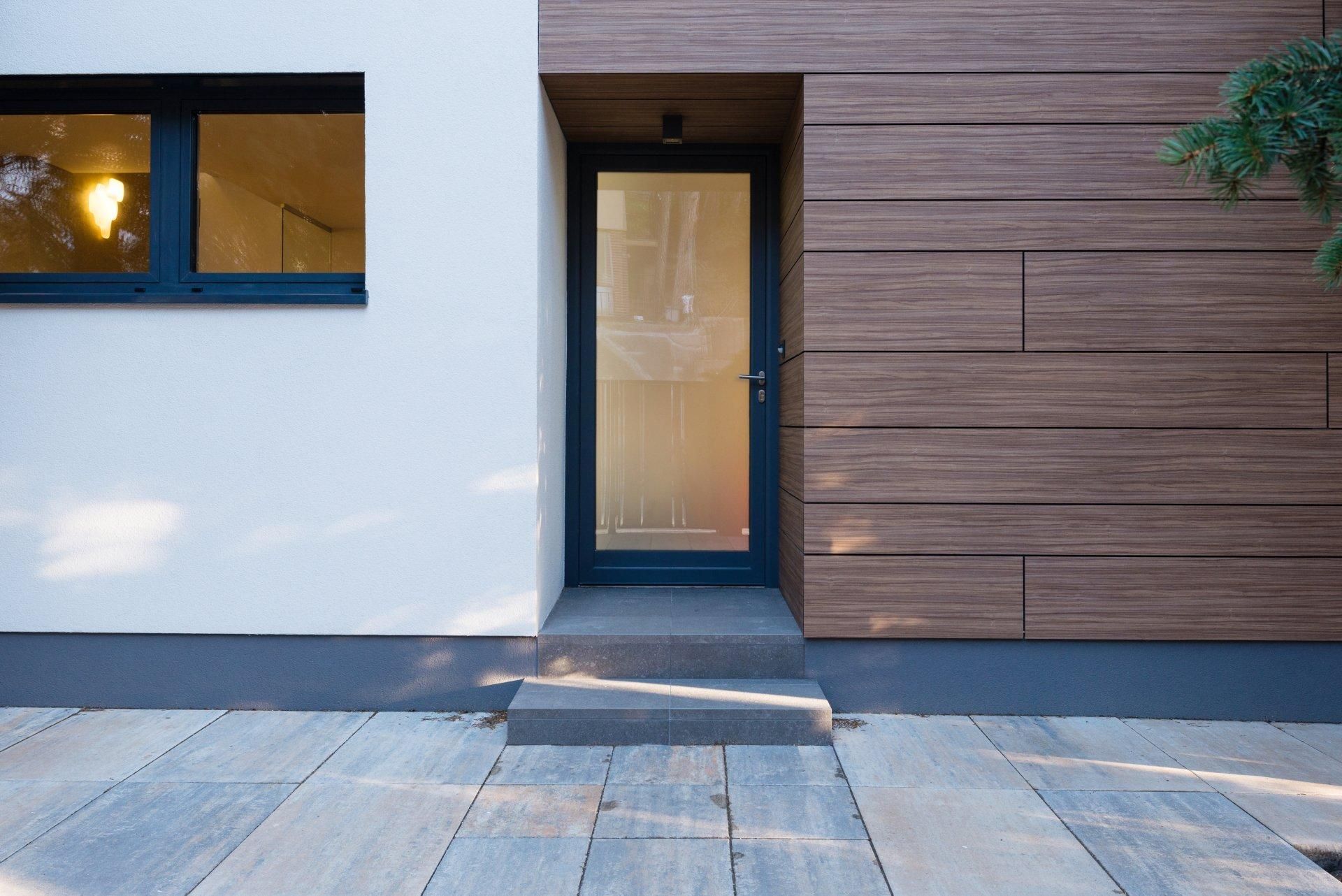 Entrée de maison moderne avec porte vitrée, mur blanc, bardage en bois et allée en pierre