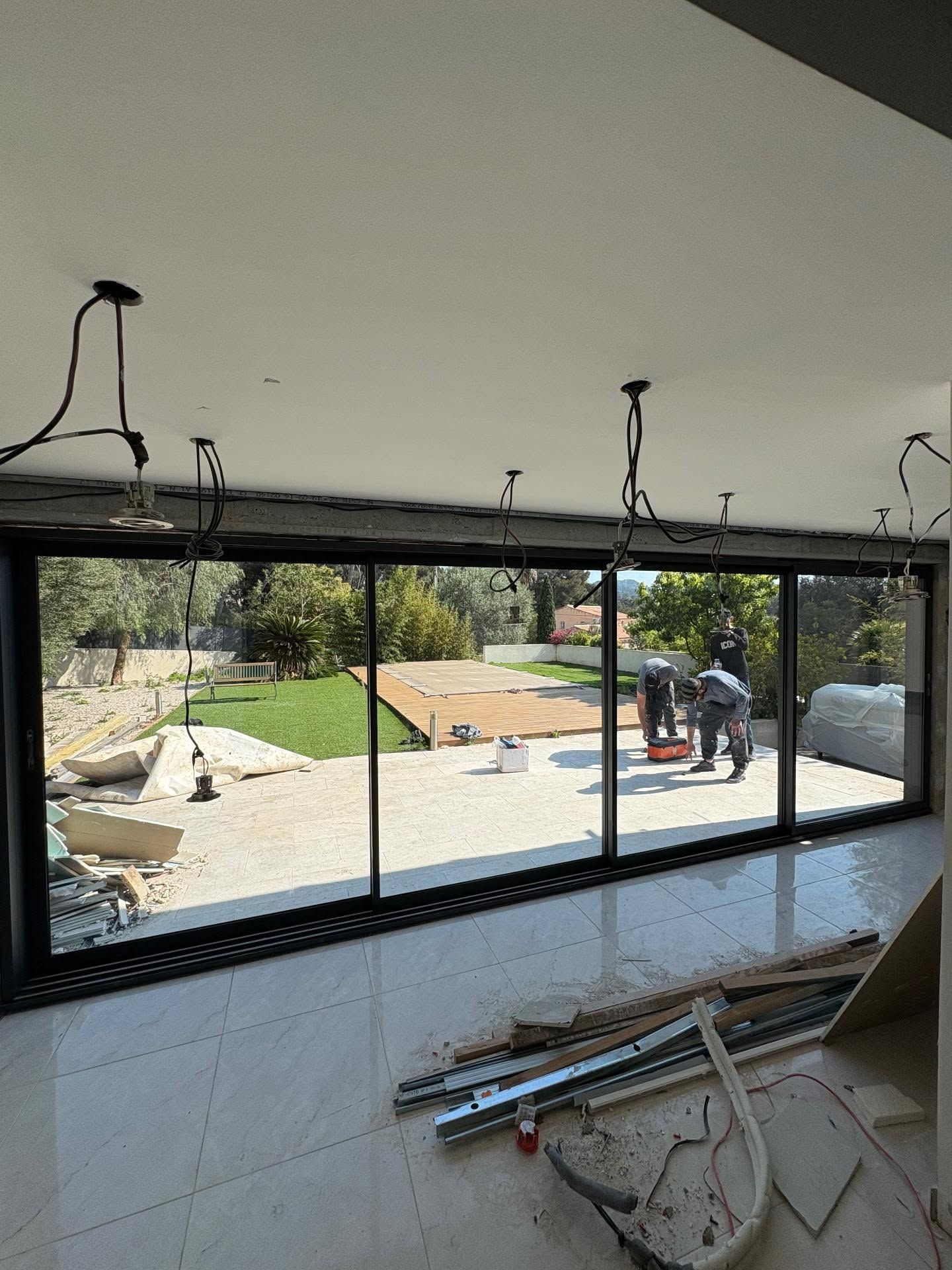 Chantier de rénovation avec une grande baie vitrée, ouvriers à l'extérieur et matériaux de construction éparpillés à l'intérieur
