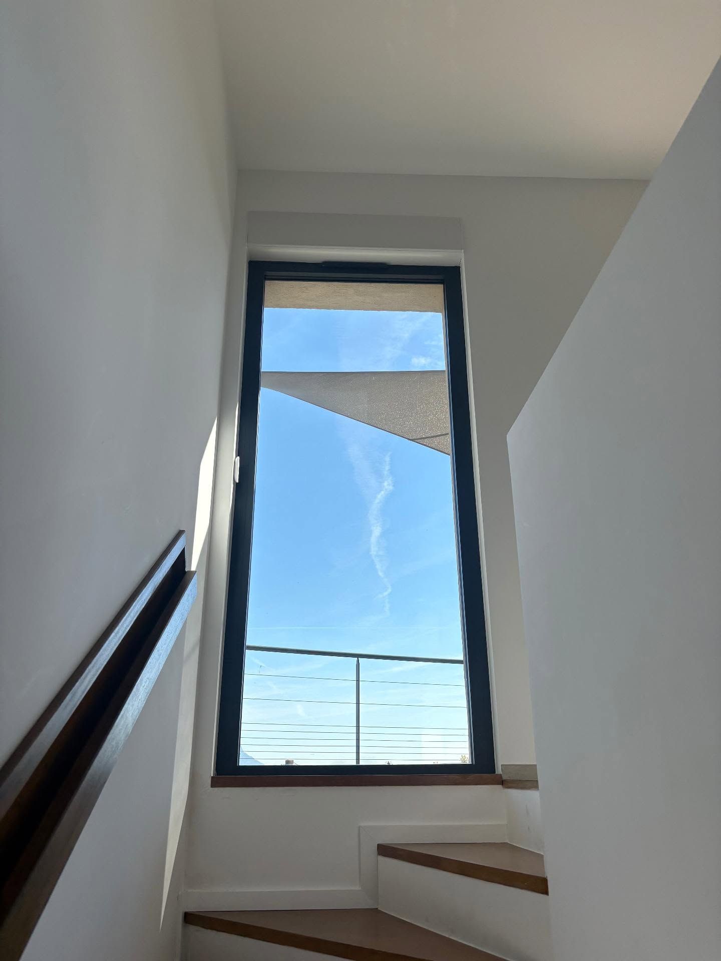 Escalier étroit aux murs blancs et à la haute fenêtre donnant sur le ciel bleu et le toit.