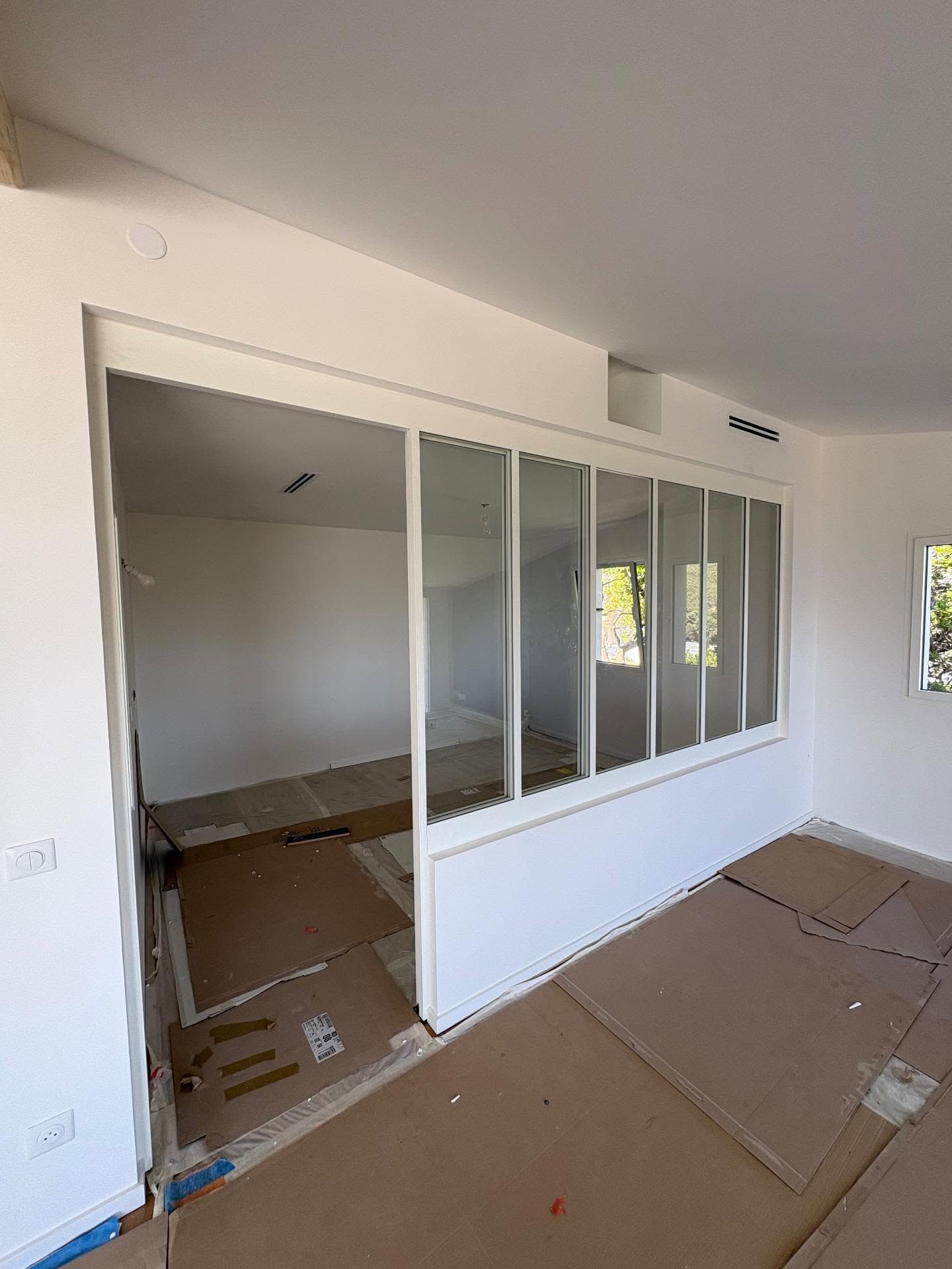 Pièce vide avec cloison coulissante en verre blanc et sol recouvert de carton en cours de rénovation