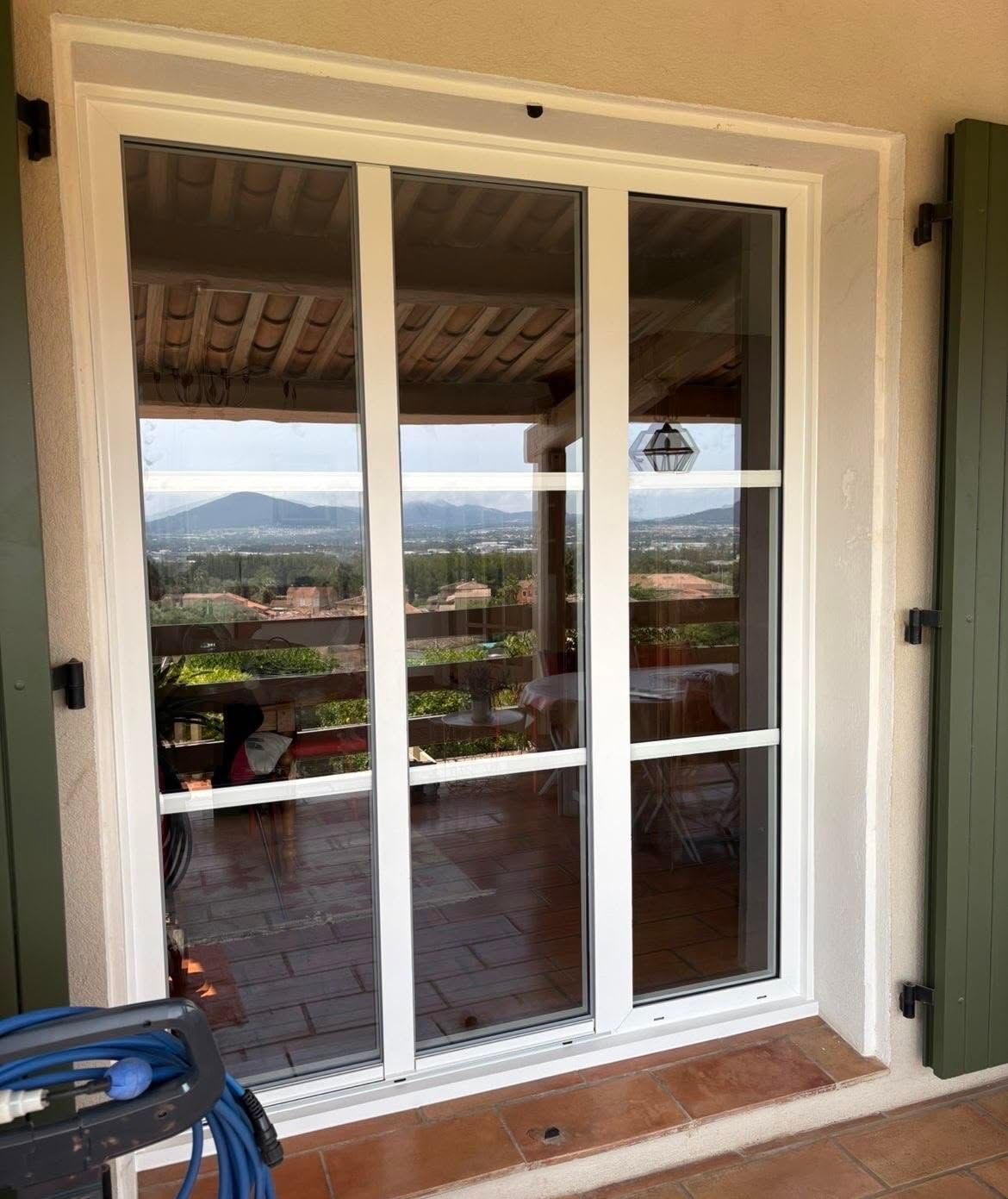 Des portes coulissantes en verre blanc s'ouvrent sur une terrasse avec vue sur les montagnes et la verdure.