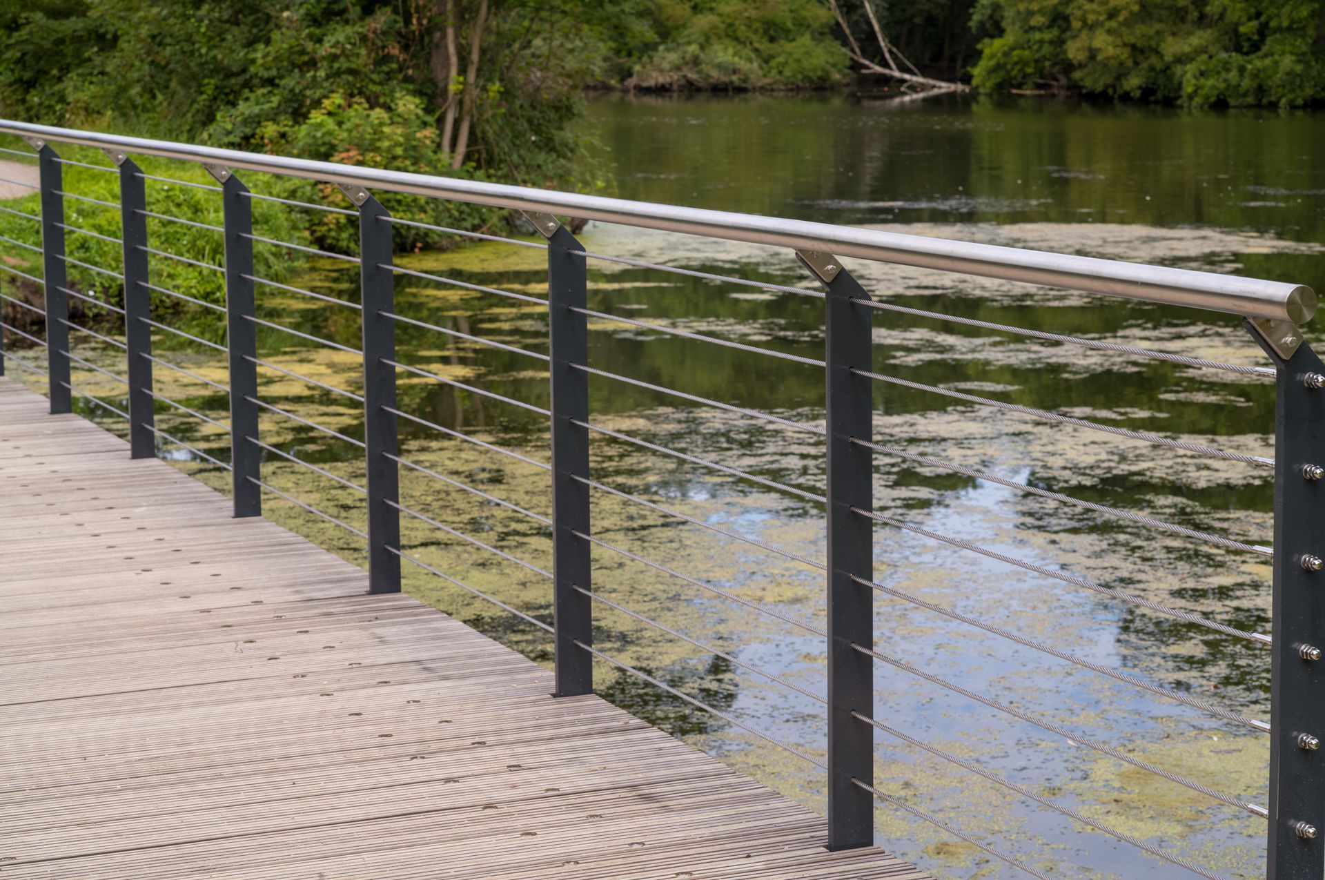 Rambarde métallique le long d'une promenade au bord de la rivière, près d'une eau calme et d'arbres