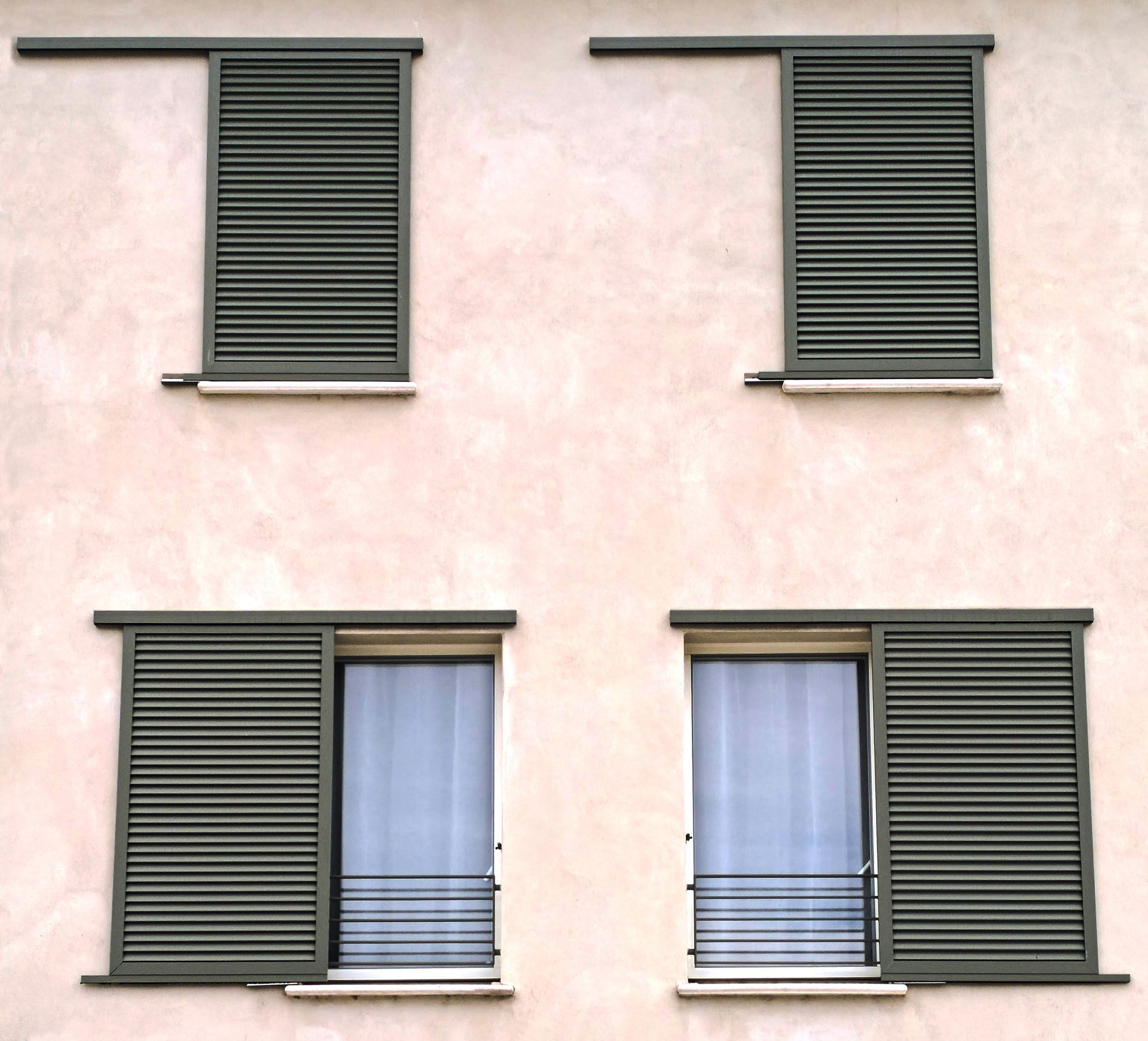 Façade d'une maison blanche avec des volets verts, un banc et un arbre projetant des ombres au soleil