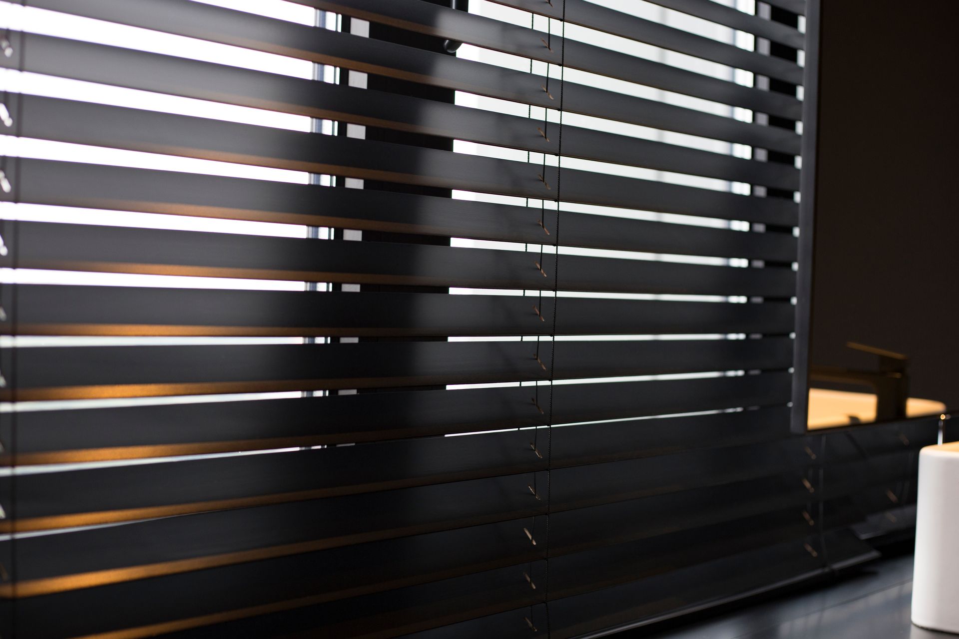 Stores noirs laissant filtrer la lumière du soleil, à côté d'une petite lampe sur un bureau