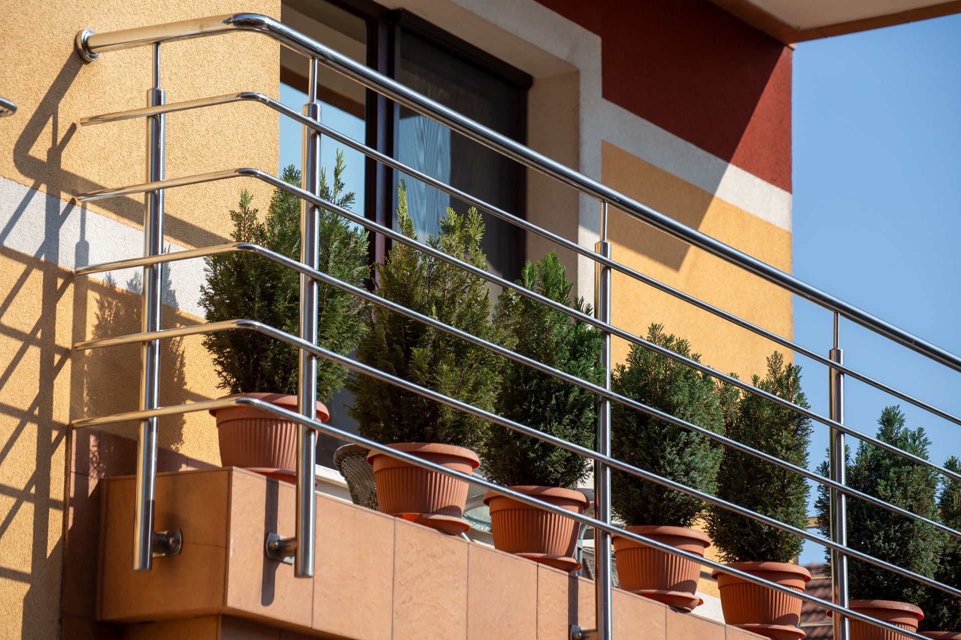 Balcon avec rambarde en métal, pots de fleurs en terre cuite et arbustes à feuillage persistant sur la façade d'un bâtiment moderne