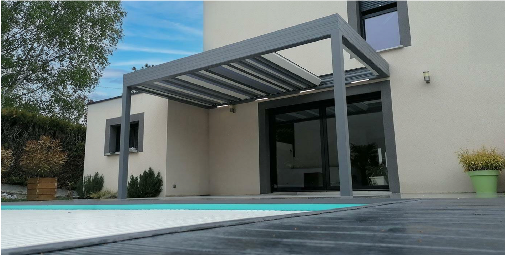 Patio moderne avec une pergola ombragée, des plantes en pot et un petit barbecue extérieur à côté d'une maison.