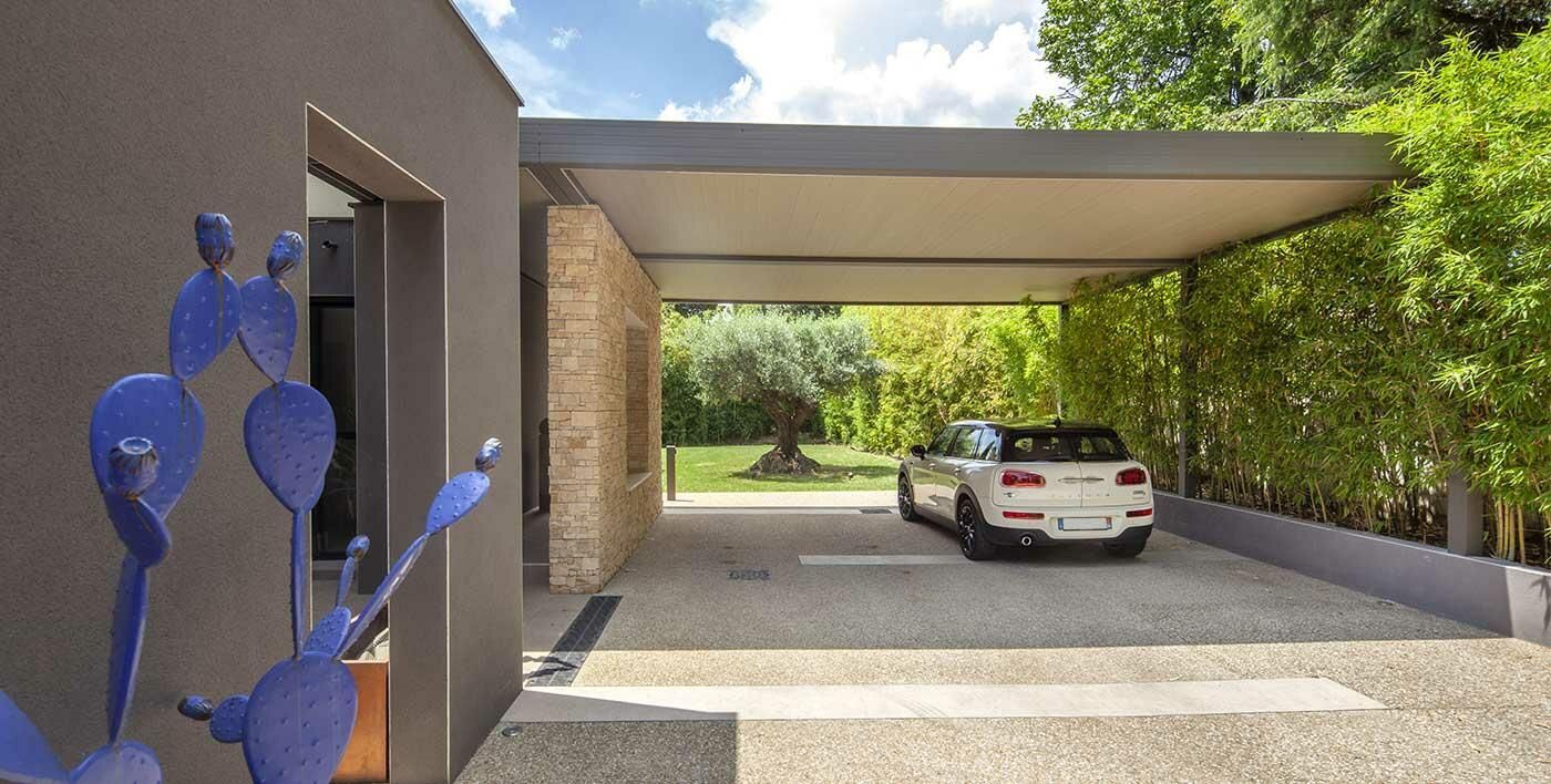 Deux voitures garées sous un abri métallique au bord d'une rue d'un quartier de banlieue