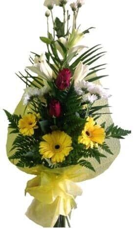 Buquê de gérberas amarelas, lírios brancos, rosas vermelhas e crisântemos brancos, embrulhado em papel de seda amarelo.